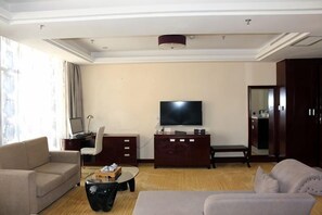 A hotel living room with a sofa, a coffee table, a TV, and a desk with a computer. - King du Hotel (Bus Station) (Nanping)