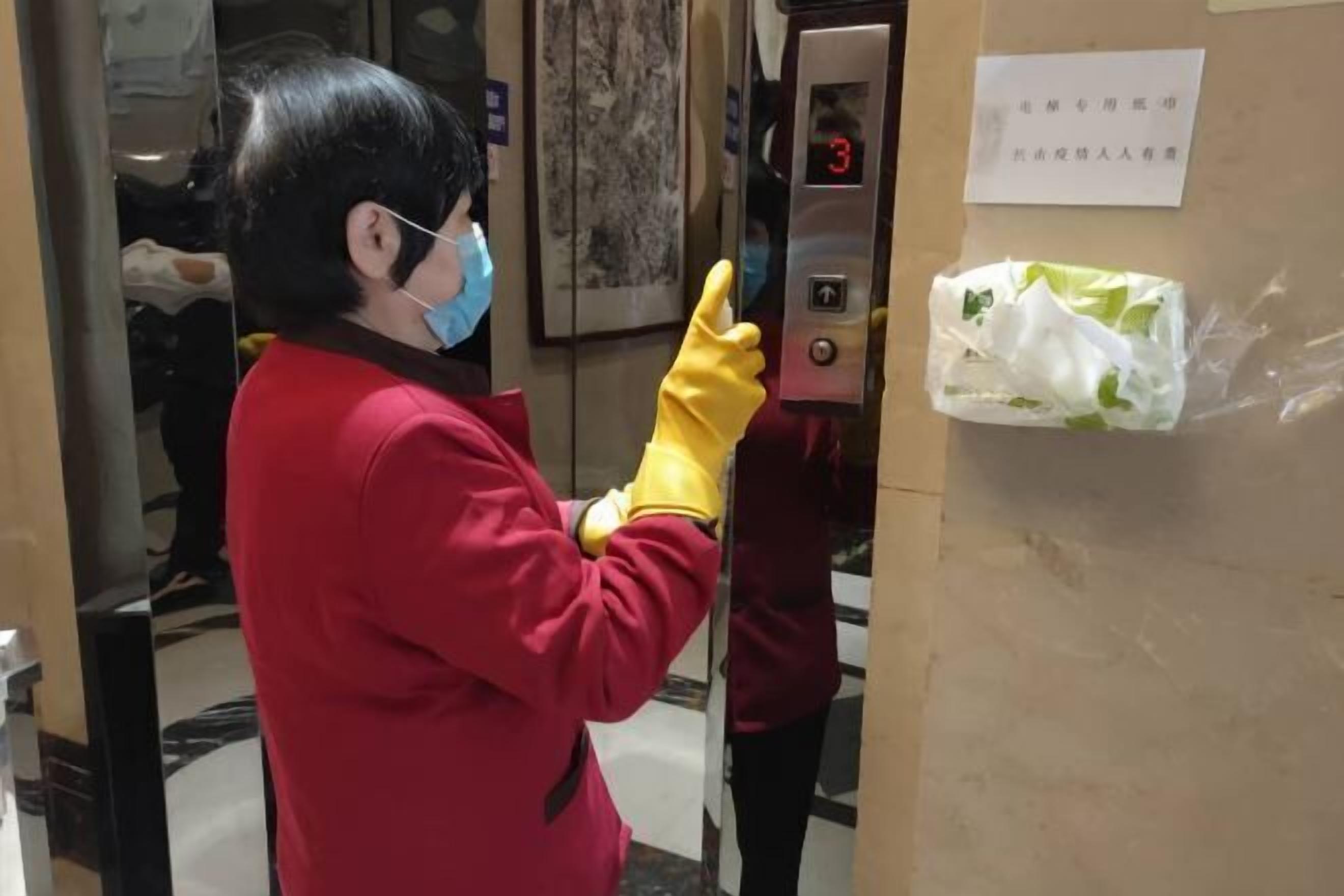 Une personne vêtue d’un uniforme rouge et portant des gants jaunes se tient à côté d’un panneau de commande d’ascenseur doté d’un écran numérique affichant le chiffre 3.