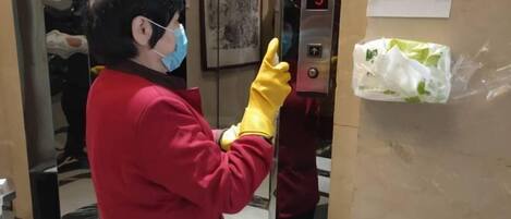Une personne vêtue d’un uniforme rouge et portant des gants jaunes se tient à côté d’un panneau de commande d’ascenseur doté d’un écran numérique affichant le chiffre 3.