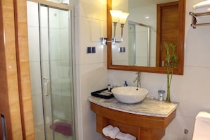 A bathroom with a glass shower enclosure, a marble sink, a wooden vanity, and a mirror with a wooden frame. - King du Hotel (Bus Station) (Nanping)