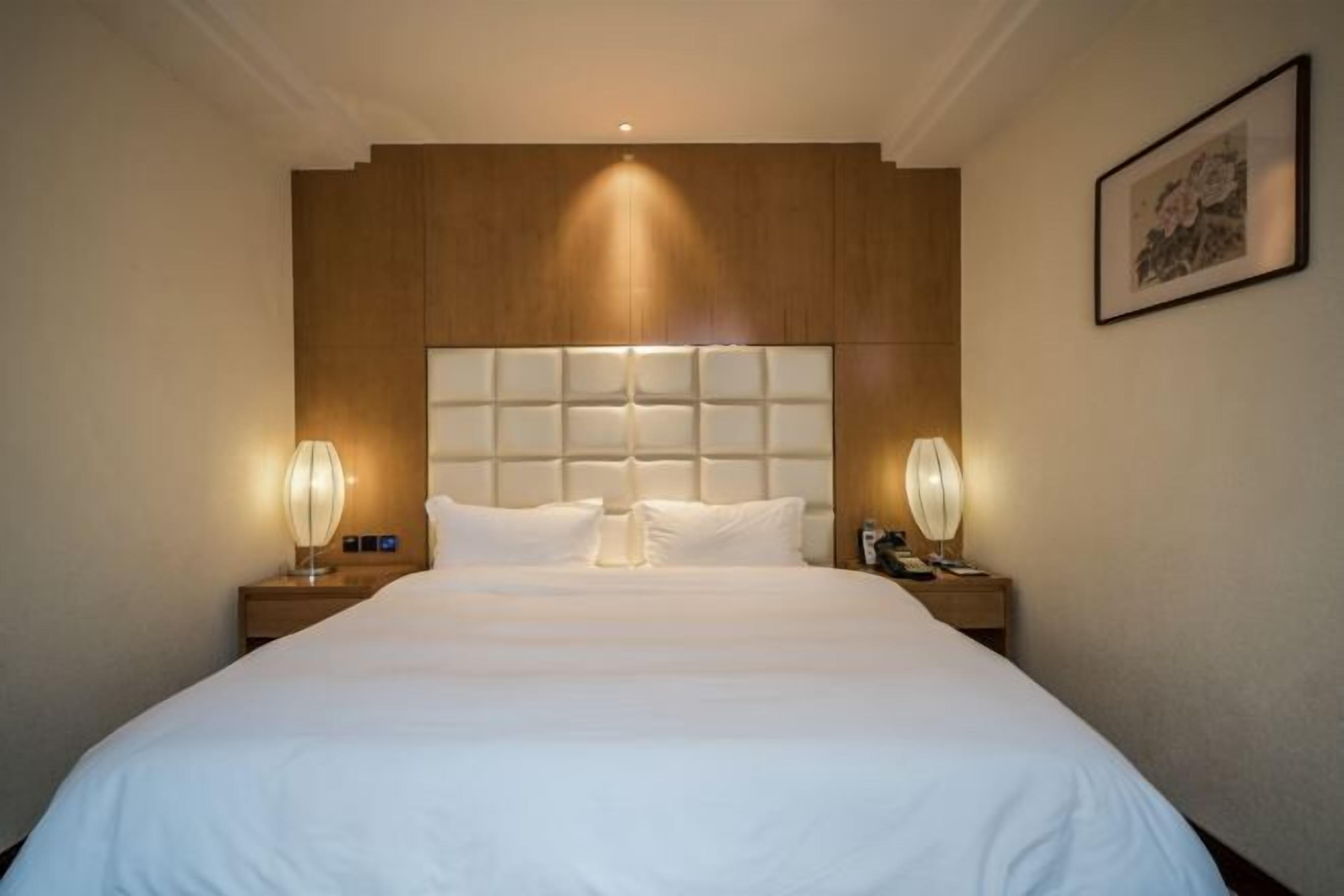Una habitación de hotel con una cama grande, cabecero de madera, lámparas de noche y un cuadro en la pared.