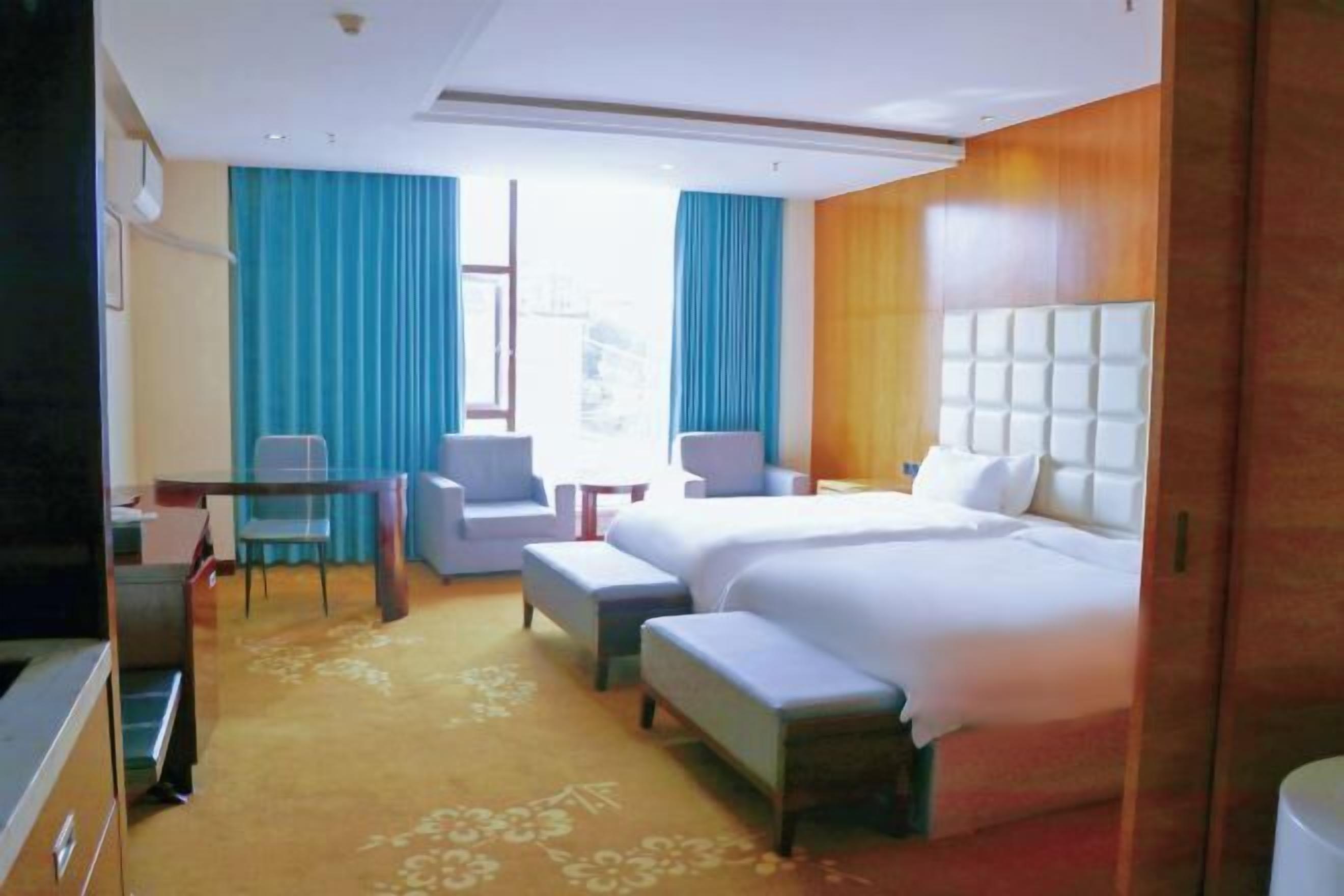 A hotel room with a large bed, two armchairs, a small table, and a TV.