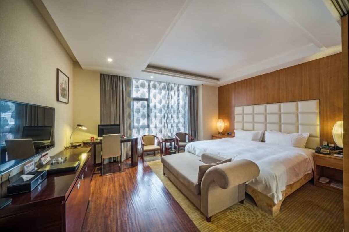 A hotel room with a bed, desk, chair, TV, and a large window.