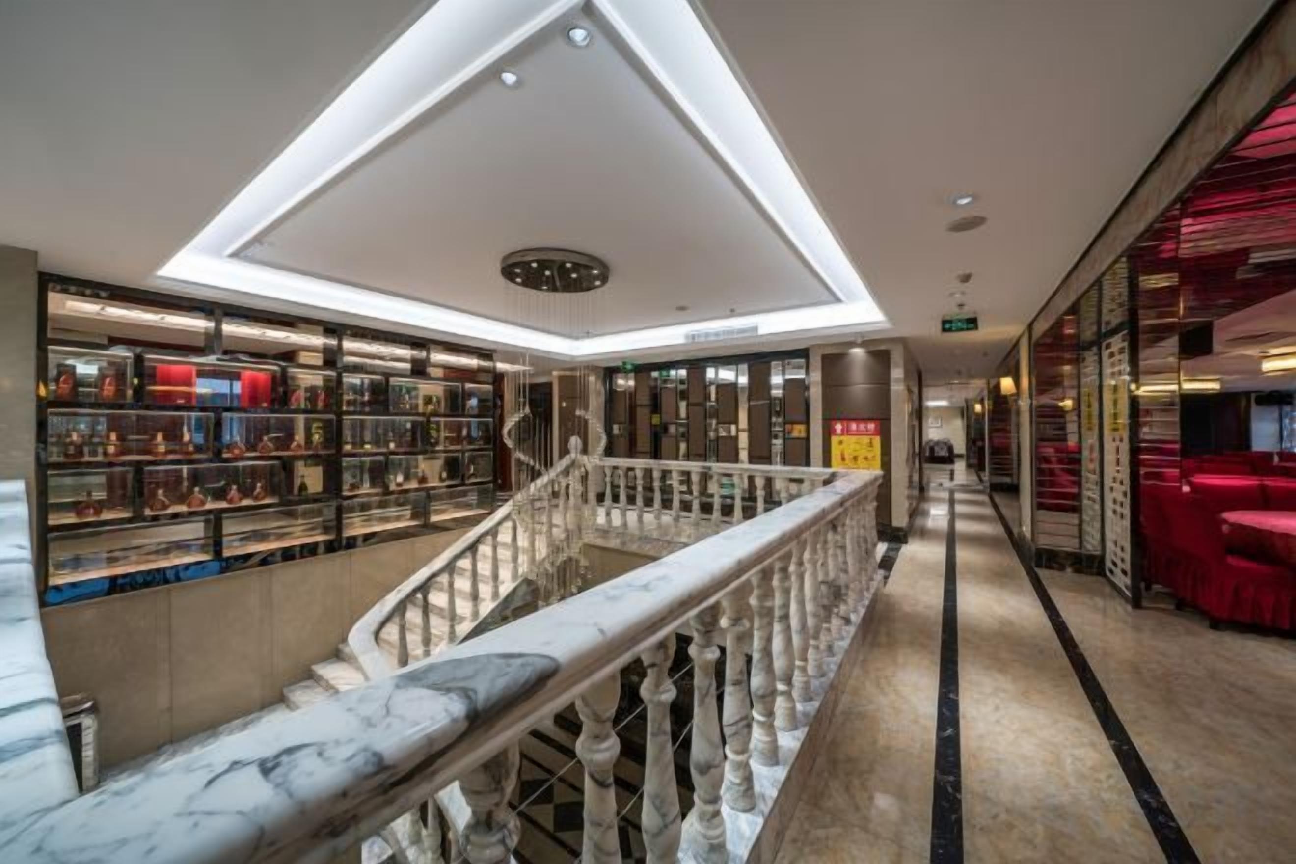 A hotel lobby with a marble staircase, a ceiling with recessed lighting, and a display of items on the left.