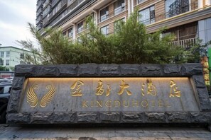 A stone sign with 'Kingdu Hotel' written in gold lettering, surrounded by greenery. - King du Hotel (Bus Station) (Nanping)