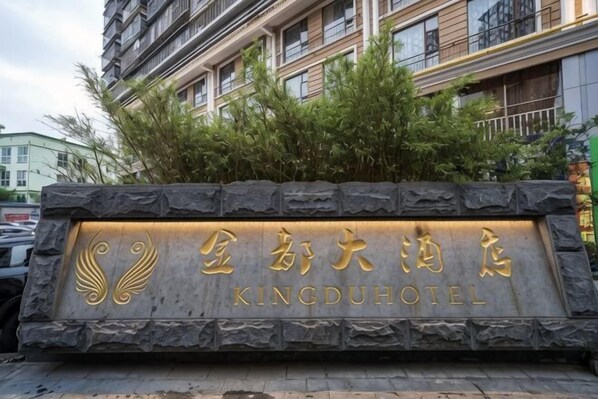 A stone sign with 'Kingdu Hotel' written in gold lettering, surrounded by greenery.