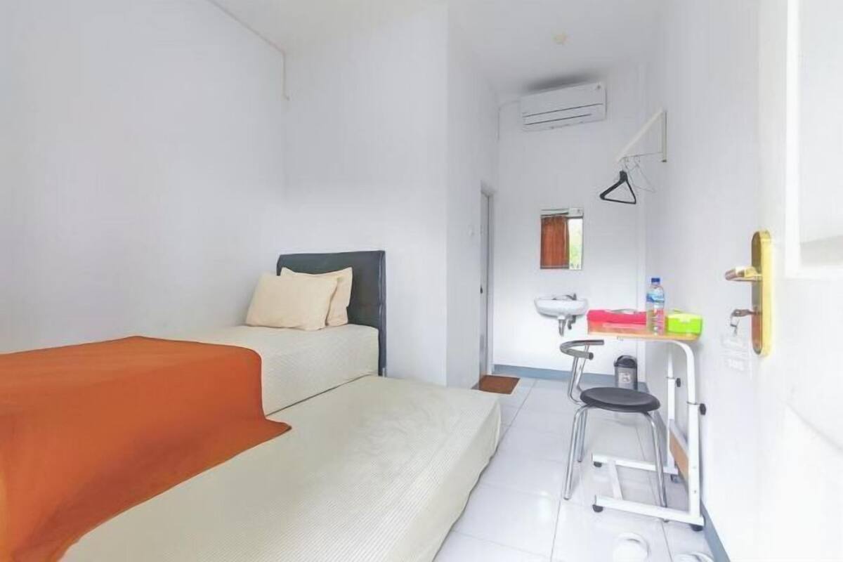 A small, bright room with a bed, a stool, a sink, and a mirror.