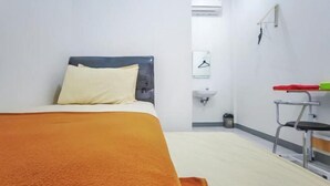 Hotellihuone, jossa on sänky, pieni työpöytä, tuoli, pesuallas ja ilmastointilaite.