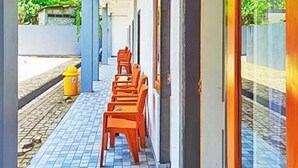 Kapea ulkokäytävä, jossa on laatoitettu lattia, puiset tuolit ja keltainen paloposti.
