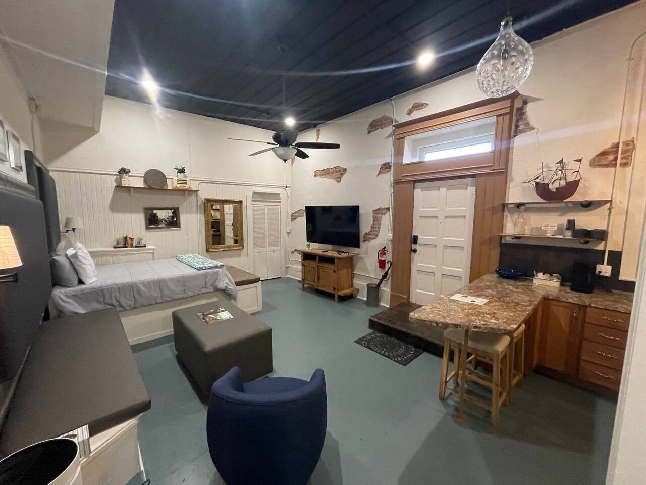 A compact living space with a bed, a seating area, a kitchen, and a television.
