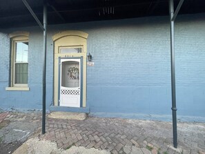 A building with a blue exterior, a white door with a decorative glass panel, and a small porch area. - The Nook at Main Street Suites (Van Buren)