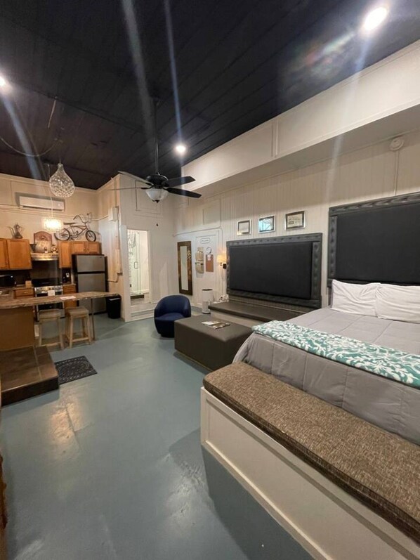 Et moderne soveværelse med en stor seng, et fjernsyn og et opholdsområde med sofa og skammel.