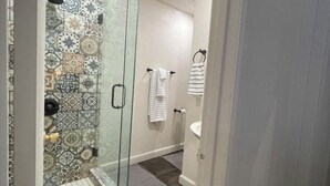 A modern bathroom with a glass-enclosed shower, patterned tiles, a white sink, and a towel rack.
