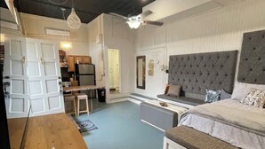 A spacious room with a large bed, a wooden desk, and a kitchenette area.