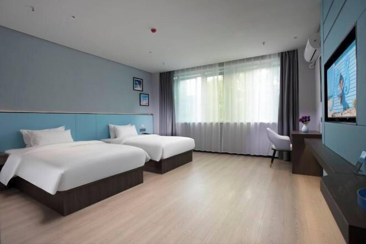 A hotel room with two beds, a desk, a chair, a TV, and a window with curtains.