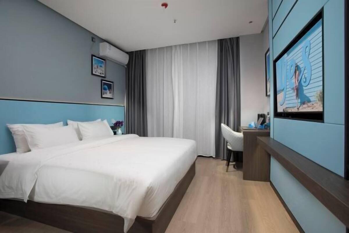 A hotel room with a bed, a desk, a chair, a TV, and a painting on the wall.