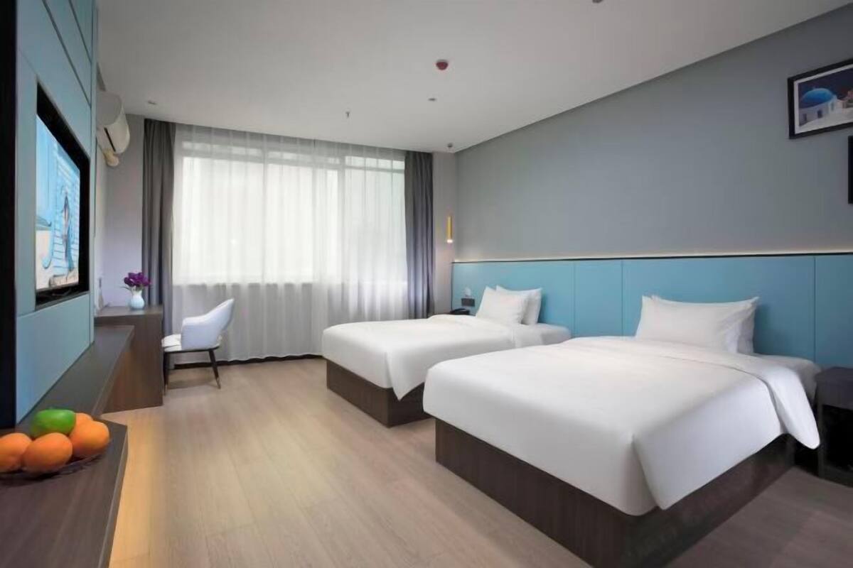 A hotel room with two beds, a desk, a chair, and a large window with curtains.