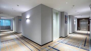 Un pasillo de hotel con piso alfombrado, una lámpara de pared y un ascensor.