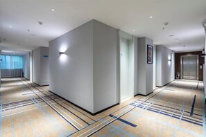 A hotel corridor with a carpeted floor, a wall-mounted light fixture, and an elevator. - Aste Meitu Hotel (Cultural Plaza Branch) (Yulin)