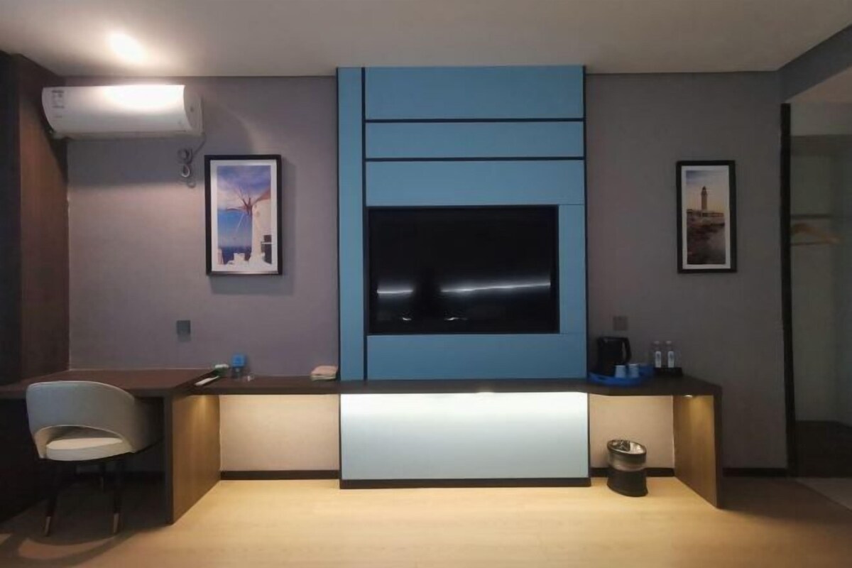 A modern room with a built-in TV, a small desk, a chair, and a trash bin.
