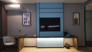 A modern room with a built-in TV, a small desk, a chair, and a trash bin.