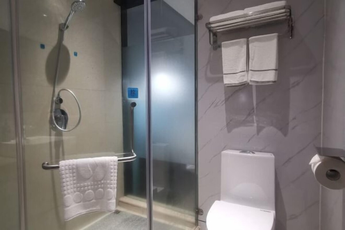 A bathroom with a glass shower enclosure, a toilet, and a towel rack with towels.