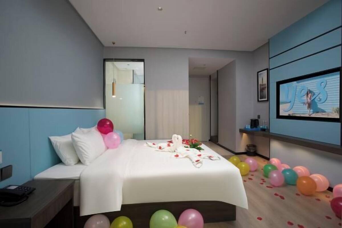 A hotel room with a bed, a bedside table, a TV, and a wall with a picture.