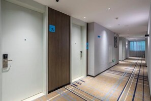 A hotel corridor with doors numbered, a carpeted floor, and a view of a window with curtains. - Aste Meitu Hotel (Cultural Plaza Branch) (Yulin)