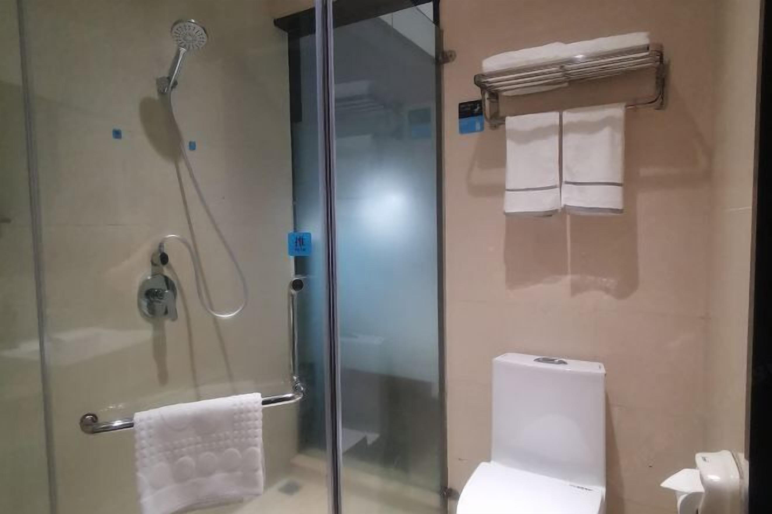 Un bagno con cabina doccia in vetro, un water e un portascopino con asciugamani.