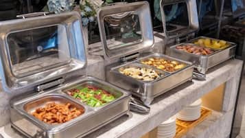 Ein Buffet mit verschiedenen Speisen in Metallbehältern, einer Marmorplatte und einem Holzboden mit Tellern.