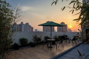 A rooftop terrace with a table and chairs, a green umbrella, and a city skyline at sunset. - Radow E Hotel (Wenzhou Chezhan Avenue Times Square Branch) (Wenzhou)