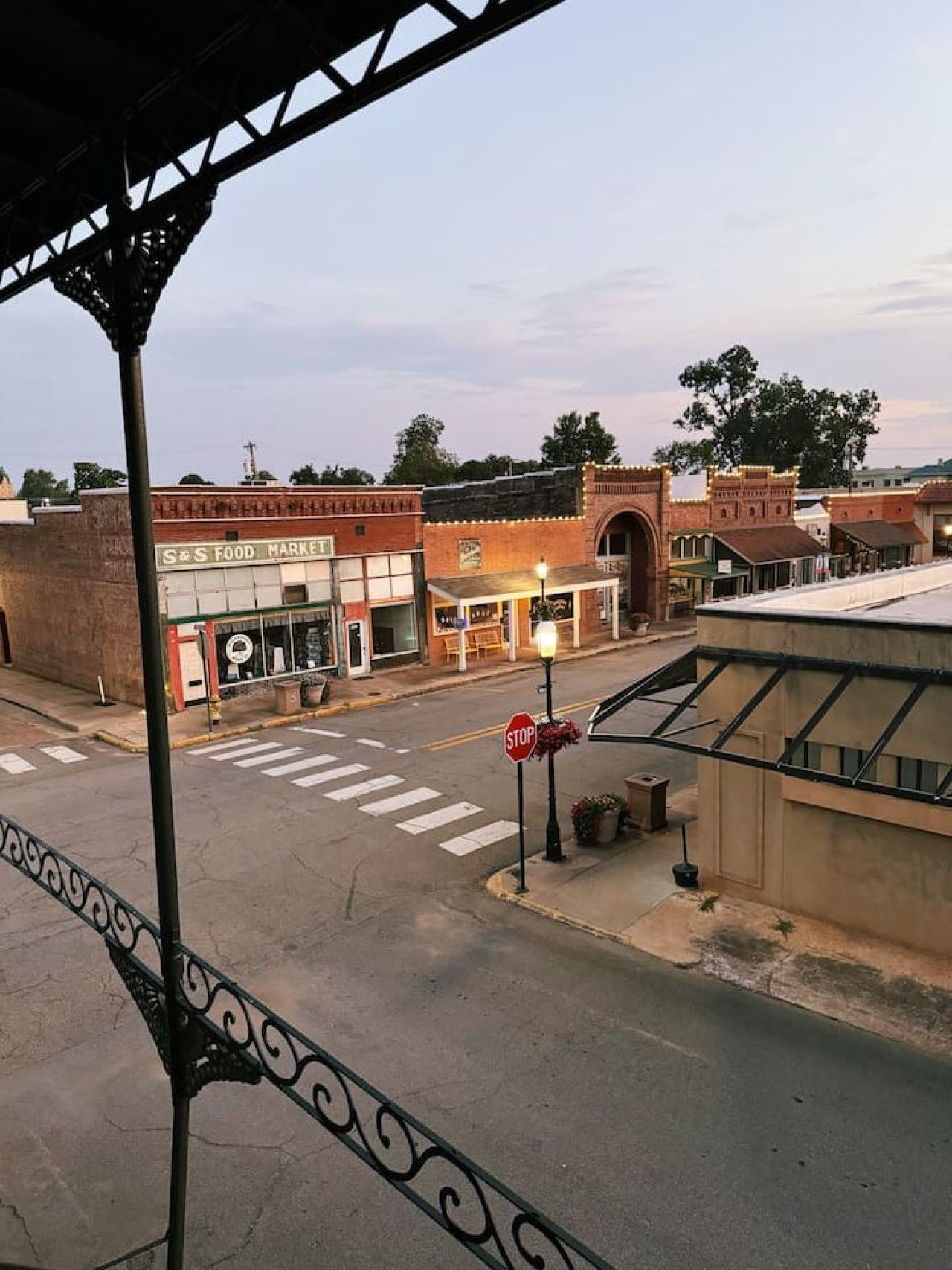 Une vue de rue avec un panneau de signalisation indiquant un arrêt obligatoire, un passage pour piétons et des bâtiments, dont un marché alimentaire.