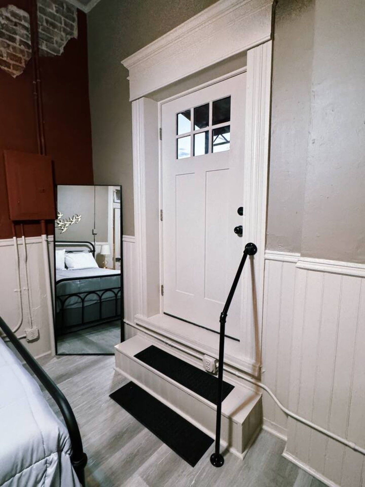 A room with a white door, a bed with a black headboard, a small window, and a black step leading to the door.
