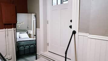 A room with a white door, a bed with a black headboard, a small window, and a black step leading to the door.