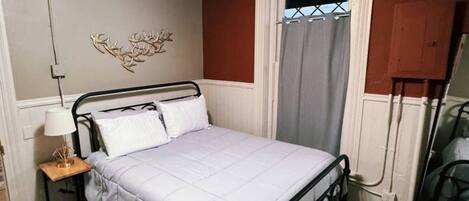 A bedroom with a bed, a ceiling fan, a wall-mounted light, a window with a curtain, and a decorative wall piece.