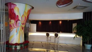 A reception area with a colorful floral mural, a reception desk, two bar stools, and potted plants. - fuerte-hotel (Yueqing)