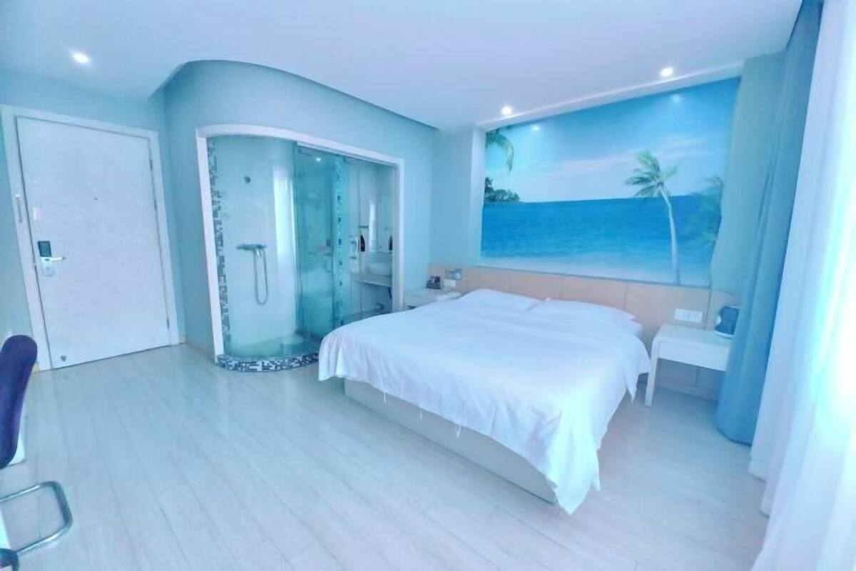 A bedroom with a bed, a walk-in shower, and a mural of a beach scene.