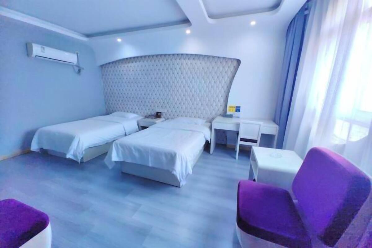 A hotel room with two beds, a desk, a chair, and a window with curtains.