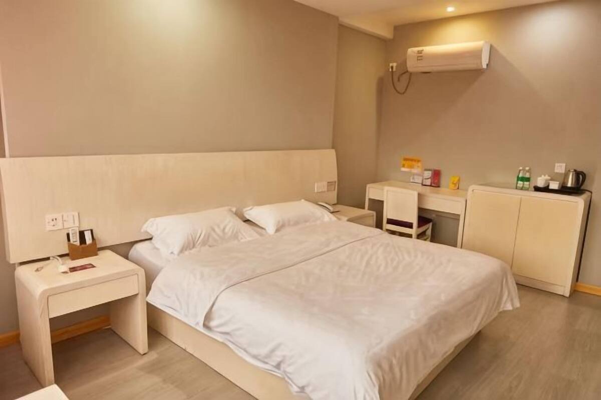 A hotel room with a bed, bedside tables, a desk, and a radiator.