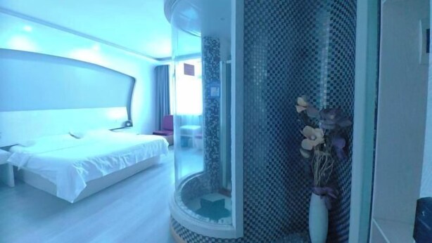 A modern hotel room with a curved glass wall, a bed, a small seating area, and a vase with flowers. - fuerte-hotel (Yueqing)
