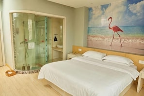 Een slaapkamer met een bed, een douchecabine van glas, een schilderij van een flamingo op een strand en een nachtkastje.