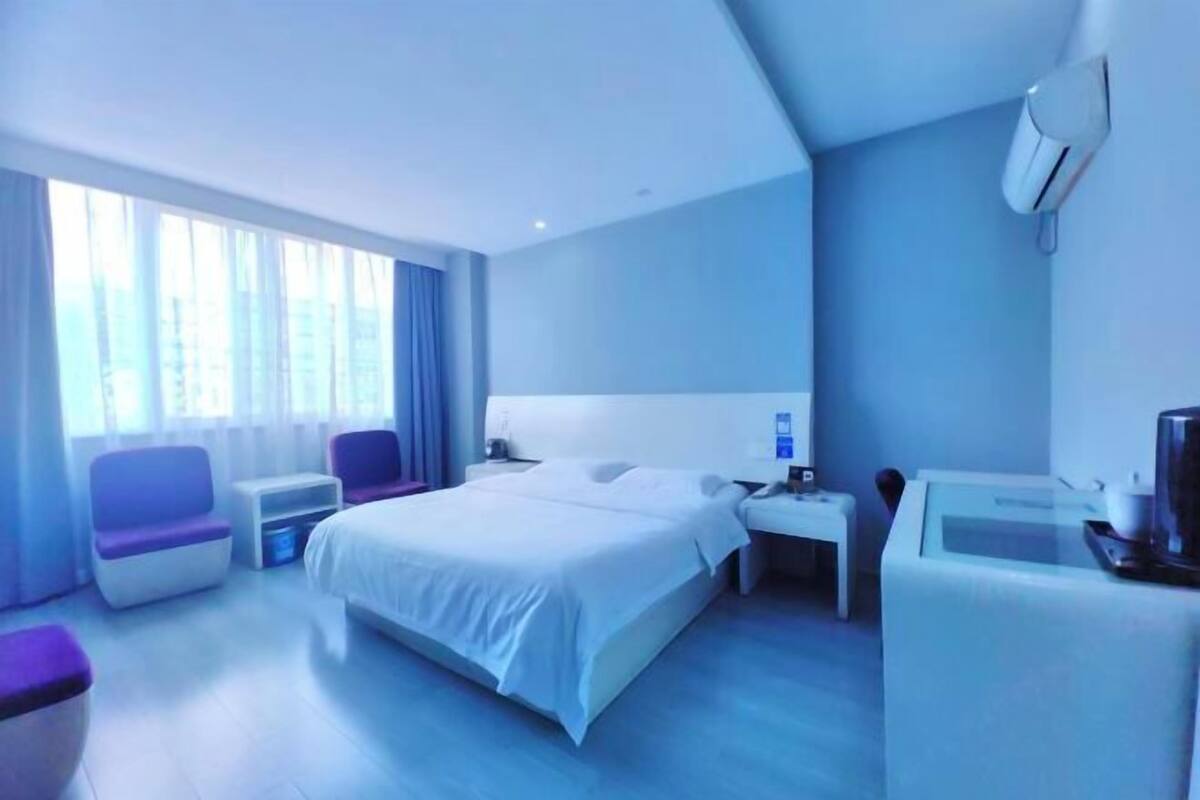 A modern hotel room with a bed, seating area, desk, and a television.
