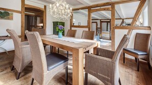 Un espace repas comprenant une table en bois, des chaises en osier, un lustre et des poutres apparentes.