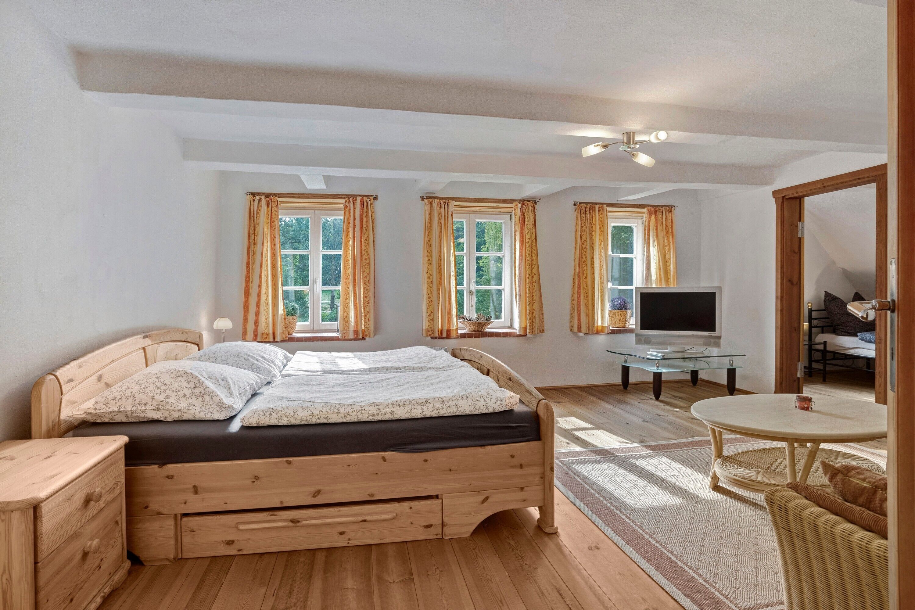 Ein Schlafzimmer mit einem hölzernen Bett, einem Fernseher, einem Glastisch und einem Korbstuhl.