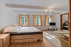 Ein Schlafzimmer mit einem hölzernen Bett, einem Fernseher, einem Glastisch und einem Korbstuhl.