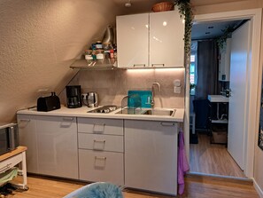 Eine kleine Küche mit Mikrowelle, Kaffeemaschine und Toaster. Ein Spülbecken mit Wasserhahn und eine Arbeitsplatte mit Gläsern und einem Korb.