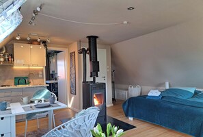 Ein gemütliches Zimmer mit einem Bett, einem Tisch mit Stühlen, einer Küchenzeile und einem Kaminofen.