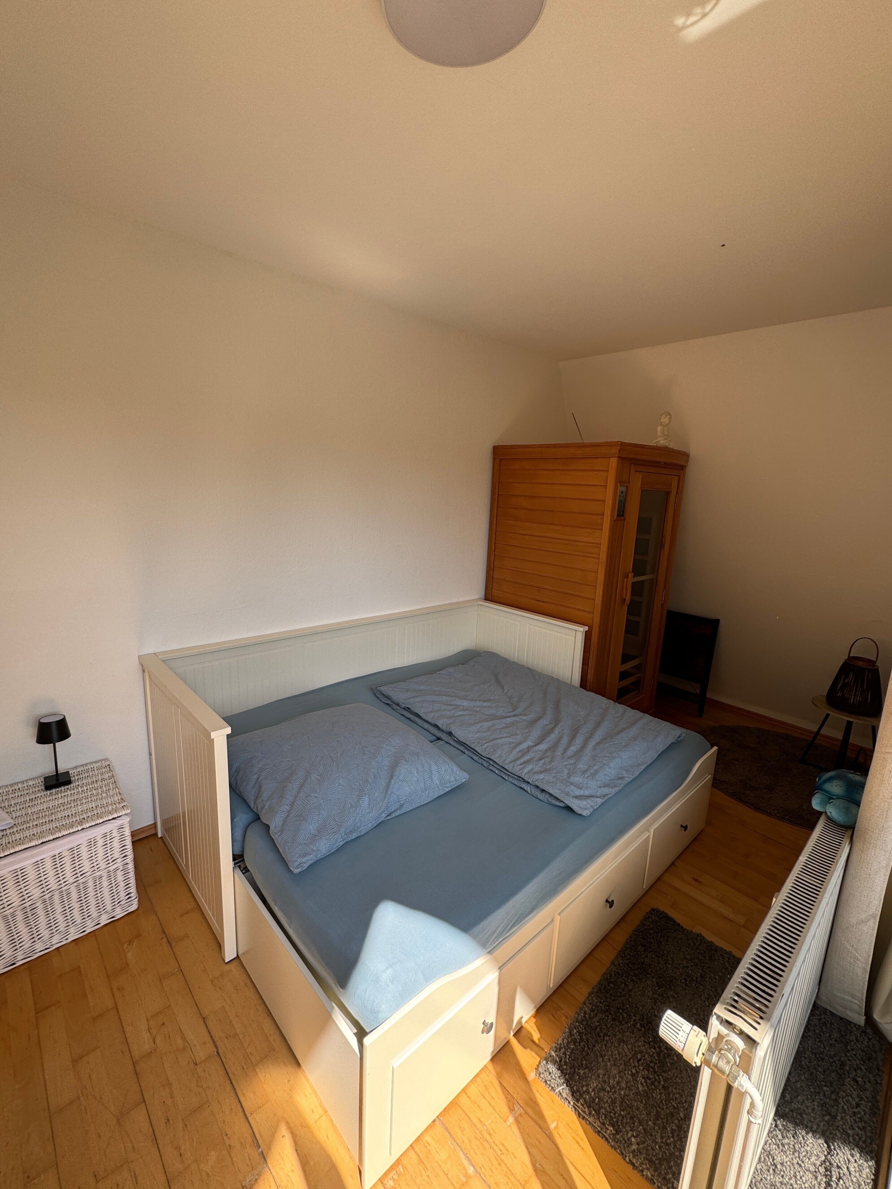 Ein Schlafzimmer mit Bett, Heizkörper, einem kleinen Schrank und einer Lampe.