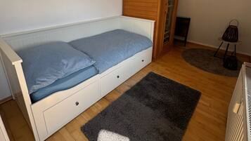 Een kleine eenpersoonskamer met een houten garderobe, een tafeltje en een radiator.