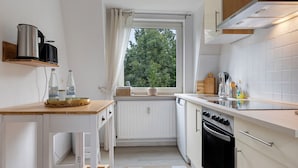A compact kitchen with a window, white cabinetry, a stove, and a sink. - Apartment 'Ferienwohnung Berti' with Balcony and Infrared Sauna (Heeßen)